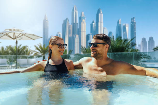 A couple relaxes in a pool with city skyscrapers in the background at DAMAC Hills 2 residential development.